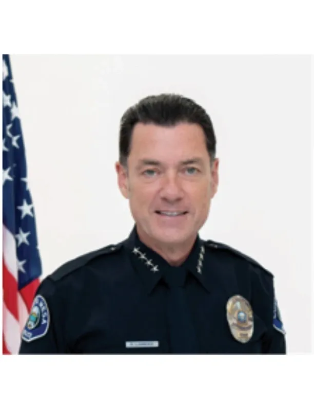 Portrait of a smiling police officer in uniform against a dark background.